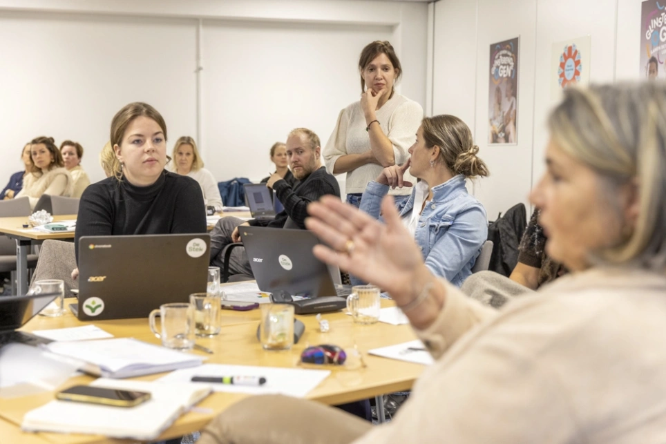 Dame in witte trui loopt door kantoortuin gevuld met discussiërende cursisten.