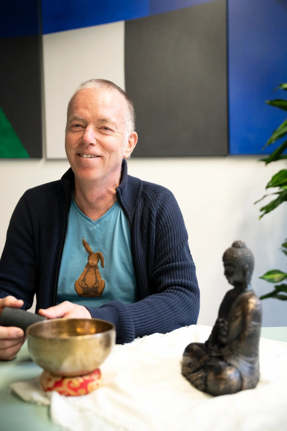 Man in baluw vest kijkt vriendelijk in camera. Naast hem een boeddhabeeld.