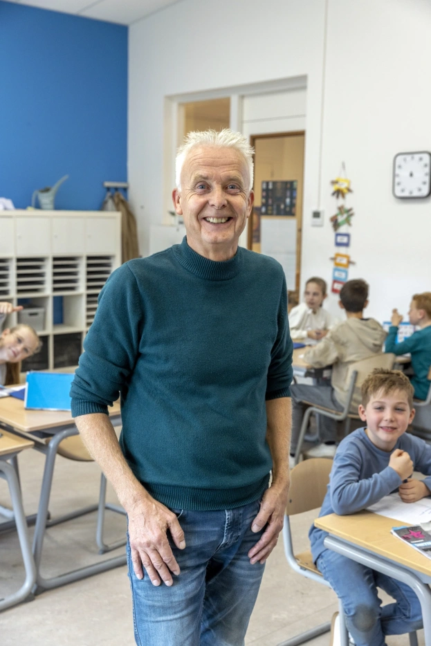 Een portret van Menno Goedhart in het klaslokaal met leerlingen op de achtergrond die aan hun tafel zitten - beeld bij AOb.nl/onderwijsblad over de vervangerspool Wonderwijs