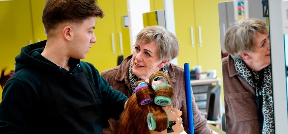 Roc Twente Kappersopleiding: Adèle Poulisse laat NT2-student Rezk Moussa zien hoe je klittenbandrollers erin draait