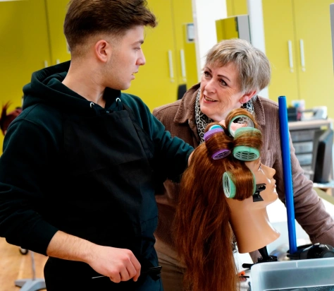 Roc Twente Kappersopleiding: Adèle Poulisse laat NT2-student Rezk Moussa zien hoe je klittenbandrollers erin draait