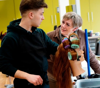 Roc Twente Kappersopleiding: Adèle Poulisse laat NT2-student Rezk Moussa zien hoe je klittenbandrollers erin draait