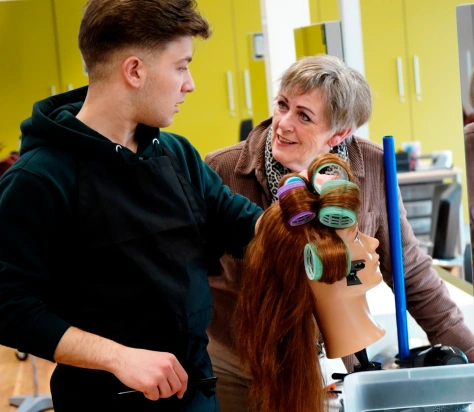 Roc Twente Kappersopleiding: Adèle Poulisse laat NT2-student Rezk Moussa zien hoe je klittenbandrollers erin draait