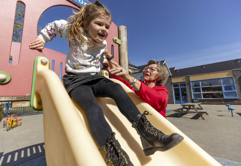 Juf Sissy helpt een kind bij de glijbaan om naar beneden te glijden op het schoolplein - Beeld bij artikel AOb.nl over doorwerken na pensioengerechtigde leeftijd