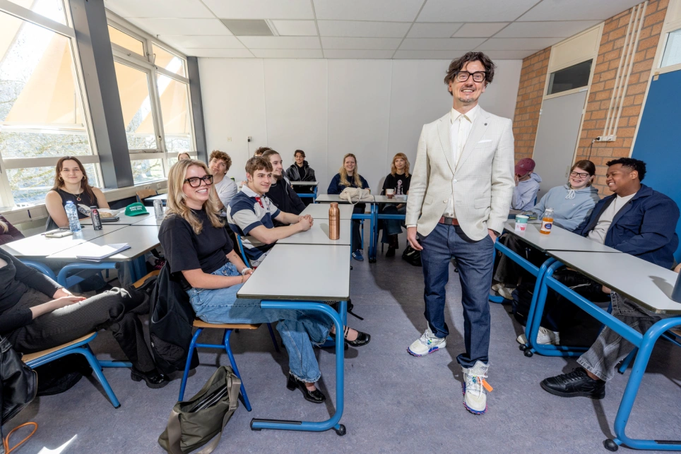 Foto van een jomge leerkracht in licht jasje en bloesje met een grote glimlach op zijn gezicht.